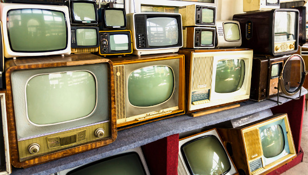 Aparelhos antigos de televisão expostos, ao lado ou em cima uns dos outros, em loja
