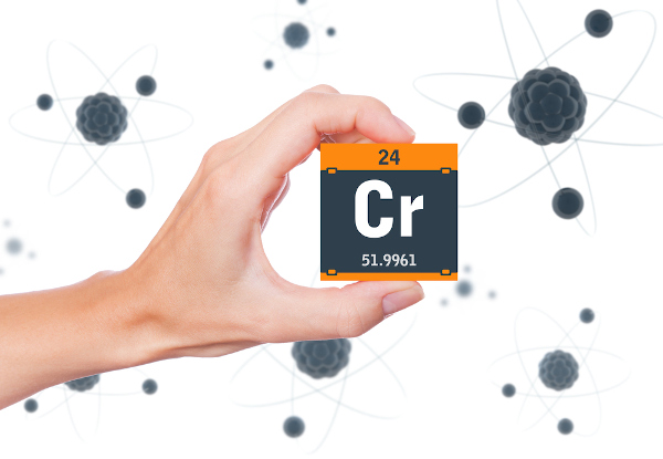 Pessoa segurando um cubo preto com laranja com o símbolo, o número atômico e a massa do elemento químico cromo.