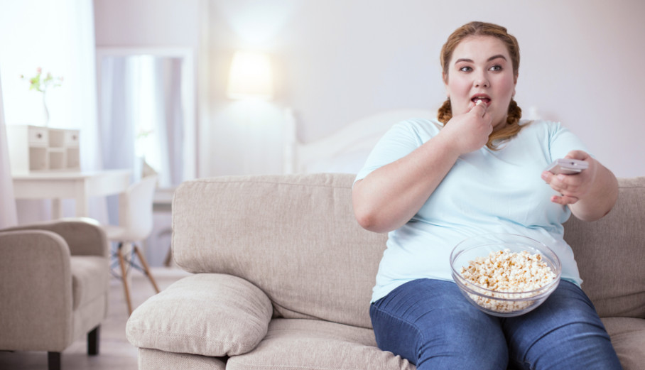 Mulher acima do peso comendo pipoca no sofá.