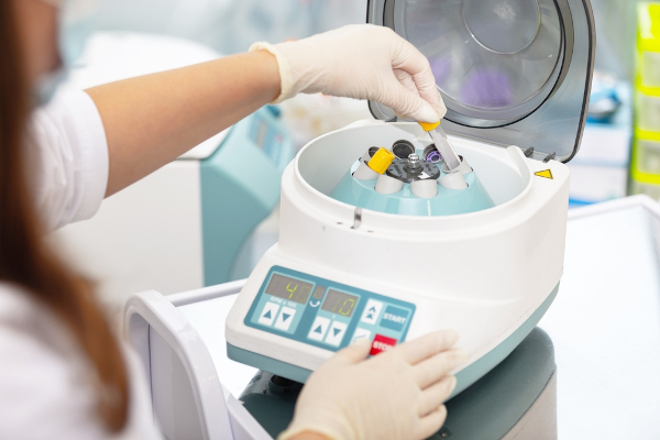 Pessoa operando uma centrífuga utilizada para realização de exames médicos em um ambiente laboratorial.