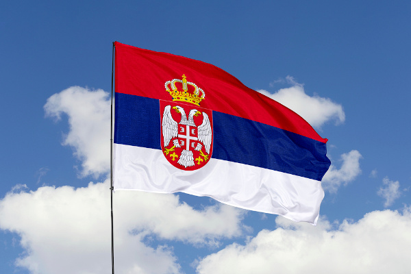 Bandeira da Sérvia hasteada e céu azul com nuvens ao fundo.