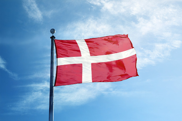 Bandeira da Dinamarca hasteada e céu azul ao fundo.