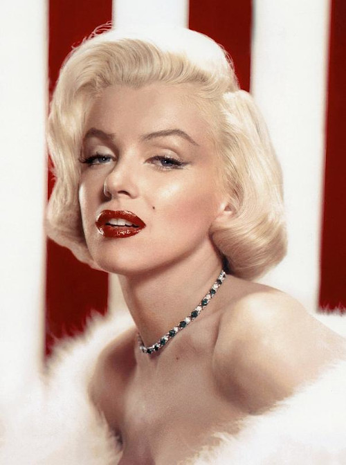 Marilyn Monroe com batom vermelho e colar usando vestido tomara que caia branco.
