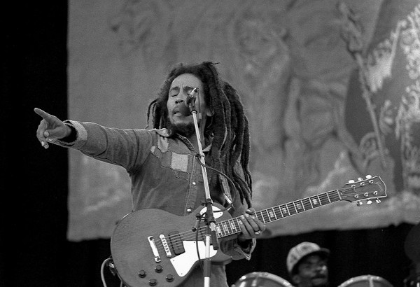 Bob Marley cantando e tocando guitarra em um show.