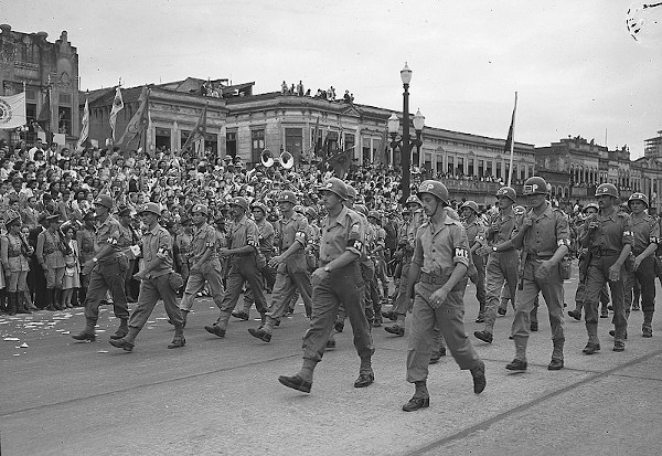 Desfile de soldados uniformizados sendo vistos pela população.