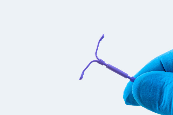 Mão enluvada segurando um DIU, pequeno objeto em formato de T, um tipo de método contraceptivo. 
