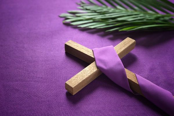 Crucifixo envolto em um tecido roxo, sobre um fundo roxo, ao lado de dois ramos.
