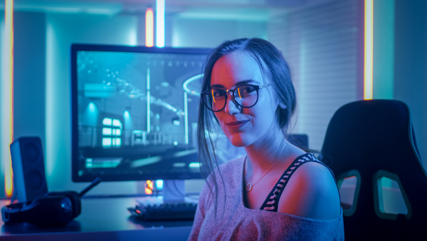 Mulher gamer com óculos em frente a um computador.