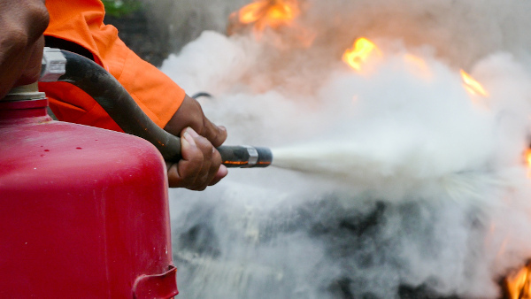 Bombeiro usando um extintor de incêndio, com bicarbonato de sódio em sua composição, para apagar um foco de incêndio.