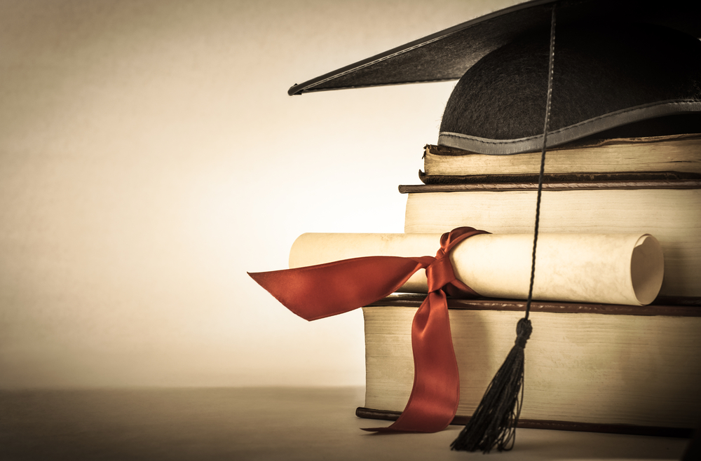 Livros empilhados atrás de um diploma e embaixo de um chapéu de formatura