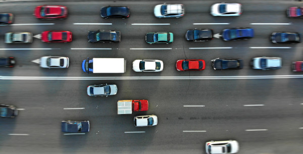 Vista superior de automóveis em uma avenida, que podem descrever movimento progressivo ou movimento retrógrado.