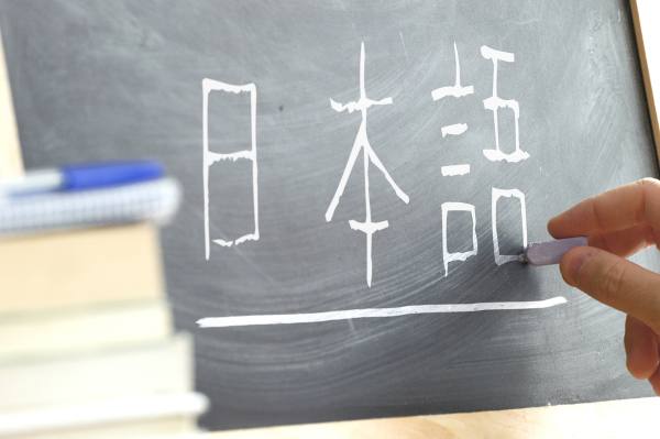 Pessoa escrevendo palavras em japonês no quadro negro.