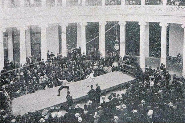Foto em preto e branco de espectadores assistindo a um combate de esgrima durante os Jogos Olímpicos (Olimpíadas) de 1906.