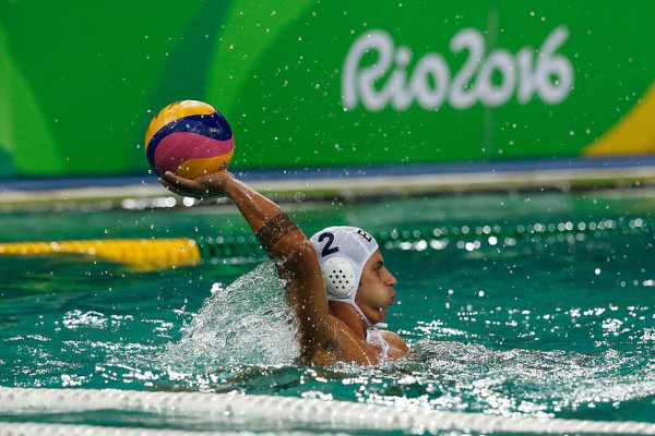 Atleta brasileiro segura bola de polo aquático durante partida.