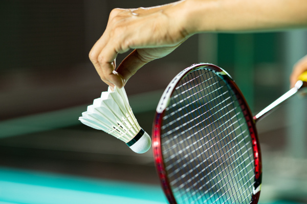 Mão posicionando peteca em uma raquete de badminton.