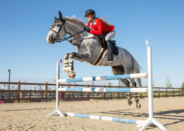 Mulher loira em prática de hipismo durante salto com cavalo.