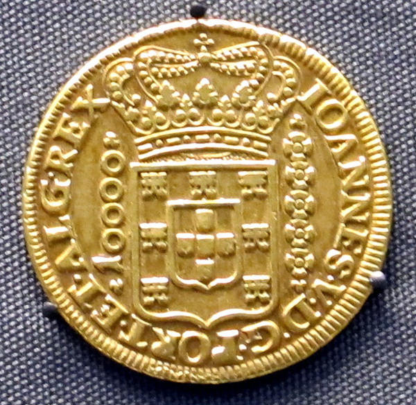 Moeda de ouro com brasão da Coroa portuguesa em texto sobre ciclos econômicos do Brasil.