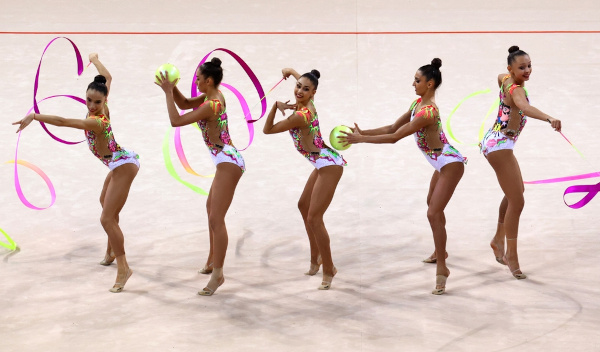 Atletas de ginástica rítmica em apresentação por equipe com uso de fitas e bolas.