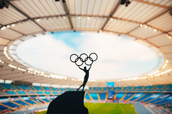 Sombra dos anéis olímpicos, com um estádio olímpico como plano de fundo, uma alusão aos Jogos Olímpicos de Verão.