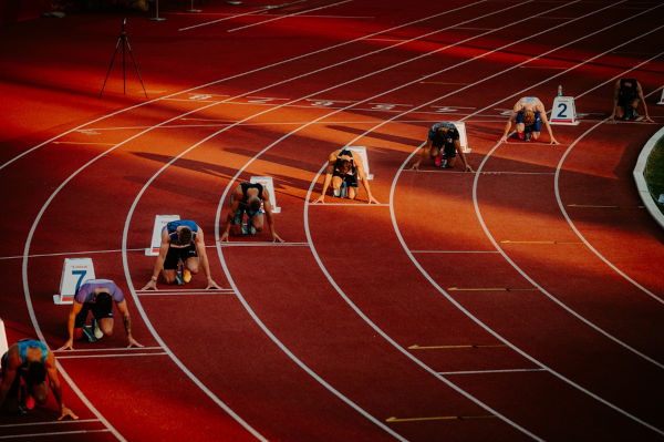 Corredores em pista de atletismo durante a largada, em texto sobre comprimento do arco.