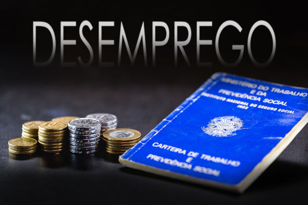 Escrito “desemprego” acima de uma carteira de trabalho e de moedas brasileiras, uma alusão ao desemprego no Brasil.