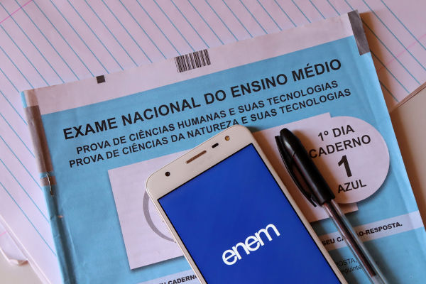 Caderno com a logo do Enem e caneta preta sobre um caderno de provas do Enem e sobre um caderno.