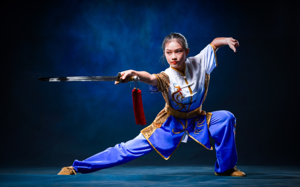 Mulher praticante de kung fu com roupa típica e em postura segurando espada. [imagem_principal]