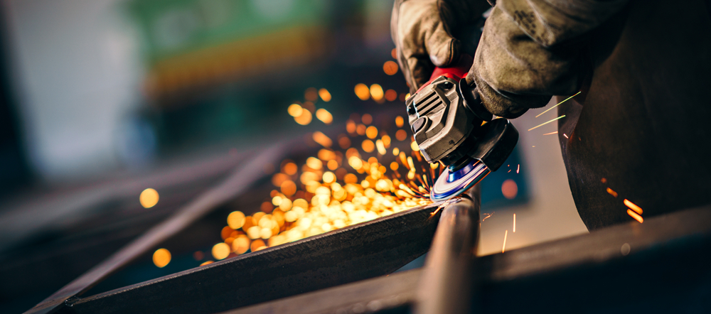 Pessoa manipulando maquinários em uma indústria pesada, responsável pelos bens de produção, que se difere dos bens e serviços.