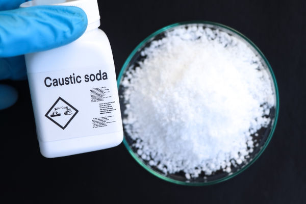 Mão segurando pote de soda cáustica, exemplo de base usada no cotidiano.