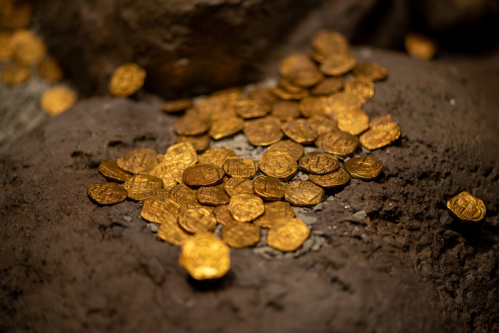 Moedas de ouro em referência ao mercantilismo, primeira fase do capitalismo. Vista interna de uma maquinofatura, essencial na segunda fase do capitalismo.