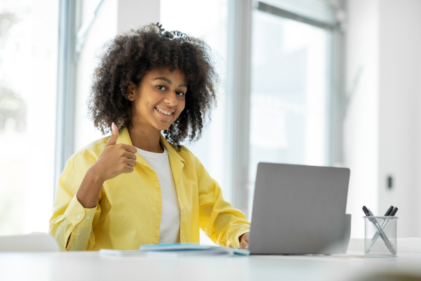 Estudante vestida com camisa amarela confere nota do Enem no notebook.