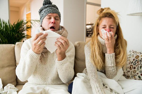 Casal assoando o nariz e espirrando, sintomas típicos de um resfriado.