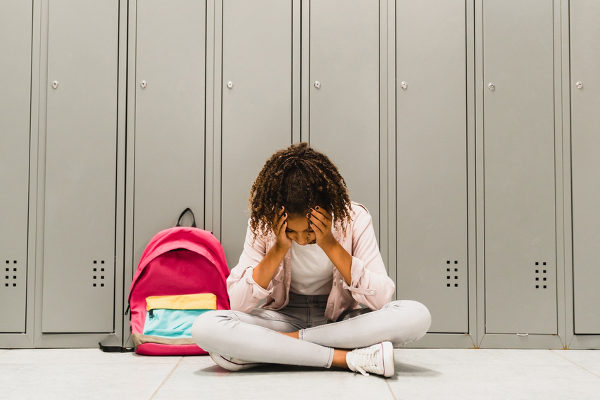 Menina negra sentada no chão da escola com a mão na cabeça