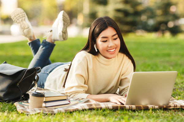 Estudante asiática deitada na grama com notebook e livros